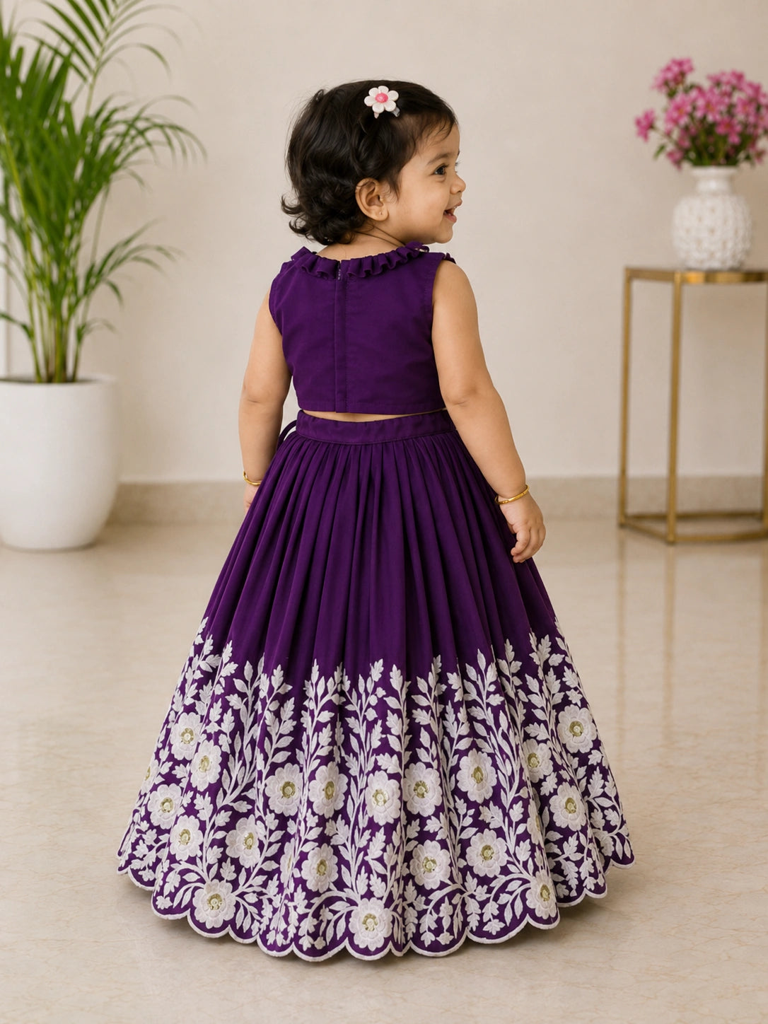 Young girl in a purple dress with floral patterns standing indoors.