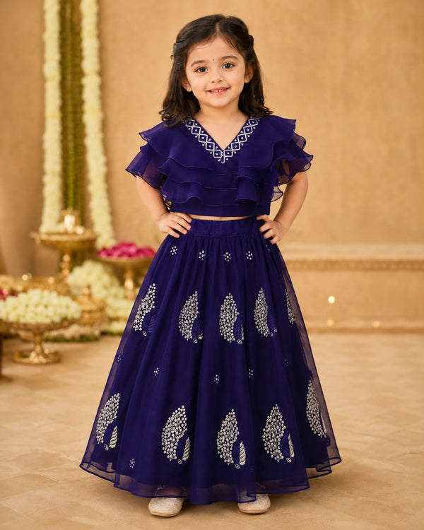 Young girl in a dark blue traditional outfit with white patterns on a decorated indoor background