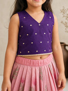 Child wearing a purple top with white patterns and a pink skirt.