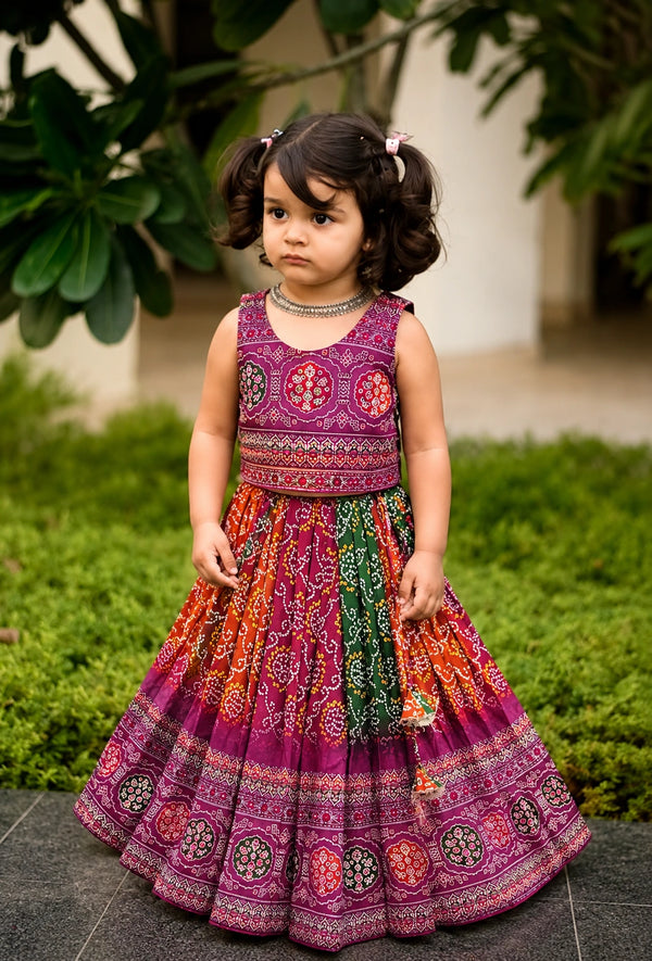 Young girl in a colorful traditional dress standing outdoors with greenery in the background