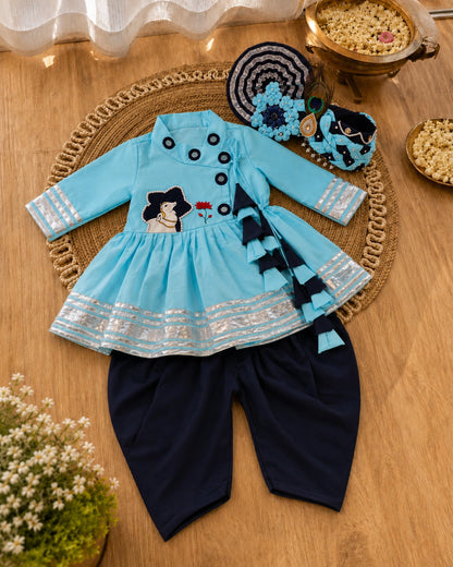 Children's outfit with a blue top and black pants on a wooden surface.